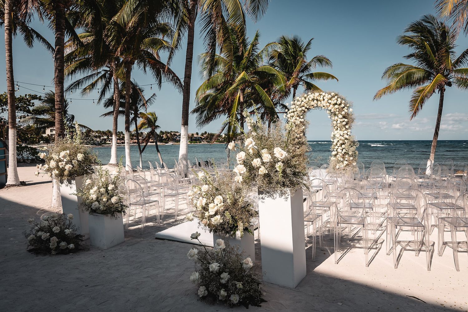 Panoramic view of a tropical beach wedding setup with white chairs and floral decorations.