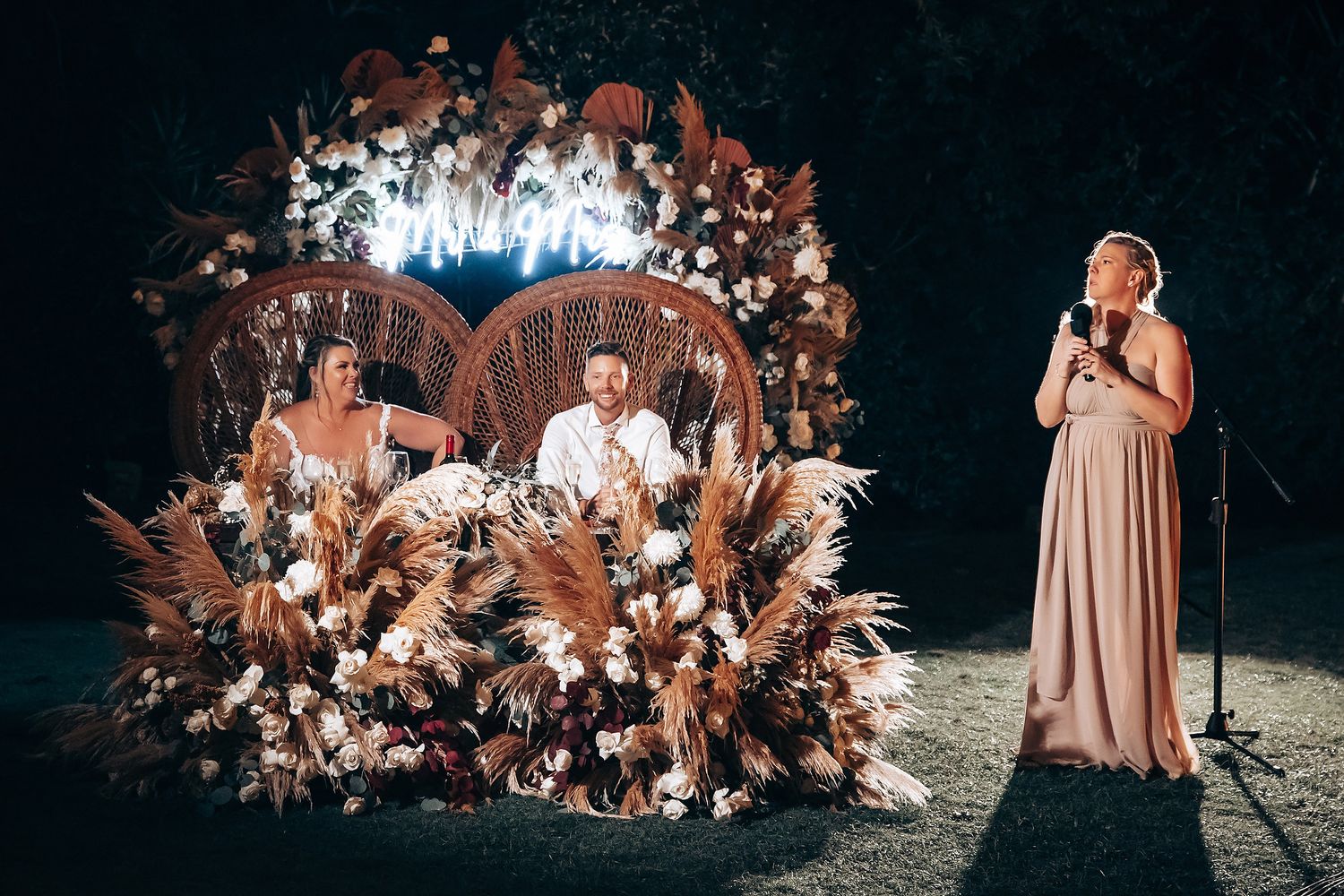 Outdoor wedding ceremony setup with dried pampas grass and floral arrangements at dusk.