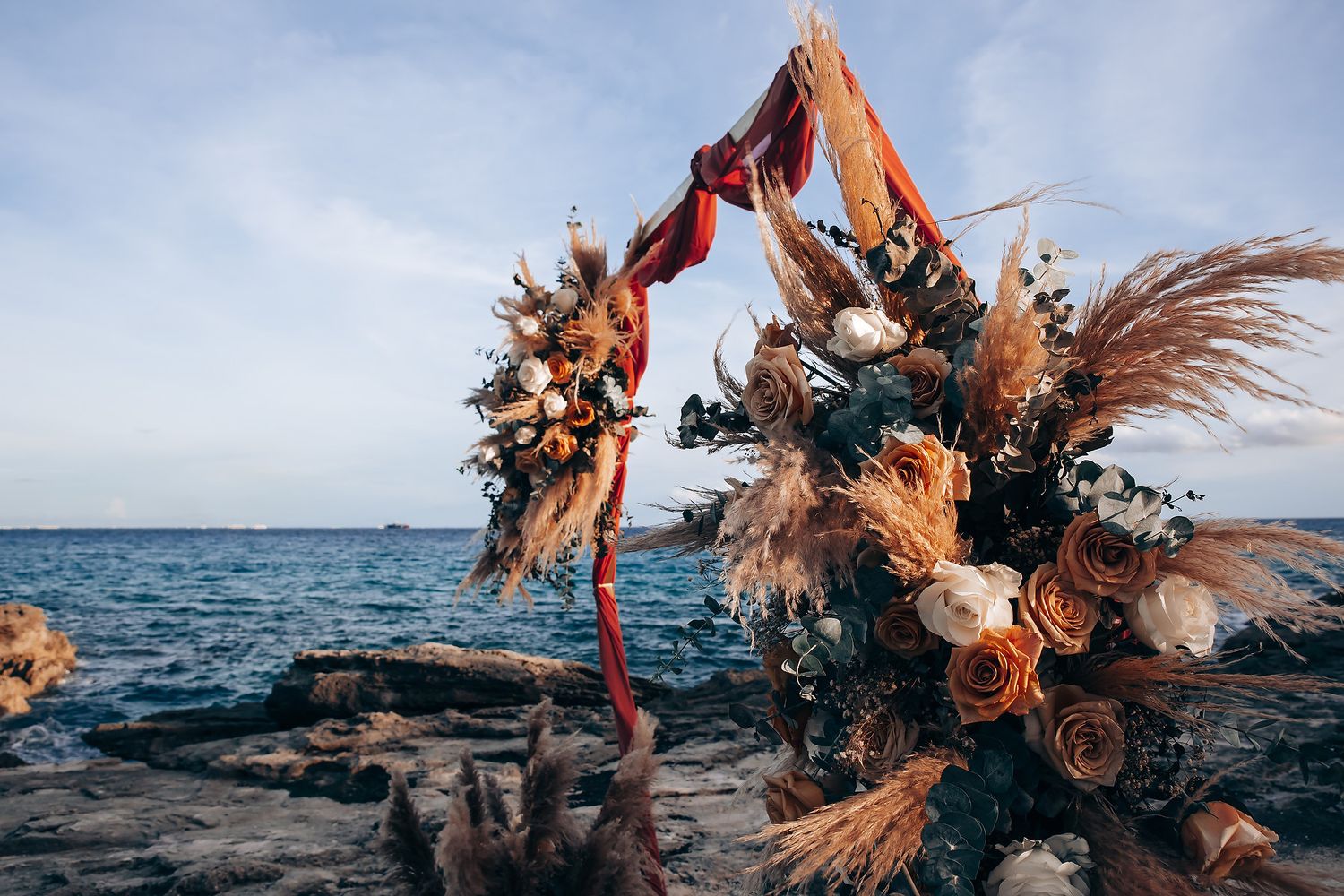 A dancer in orange costume performs an expressive dance movement against a scenic ocean backdrop at sunset.