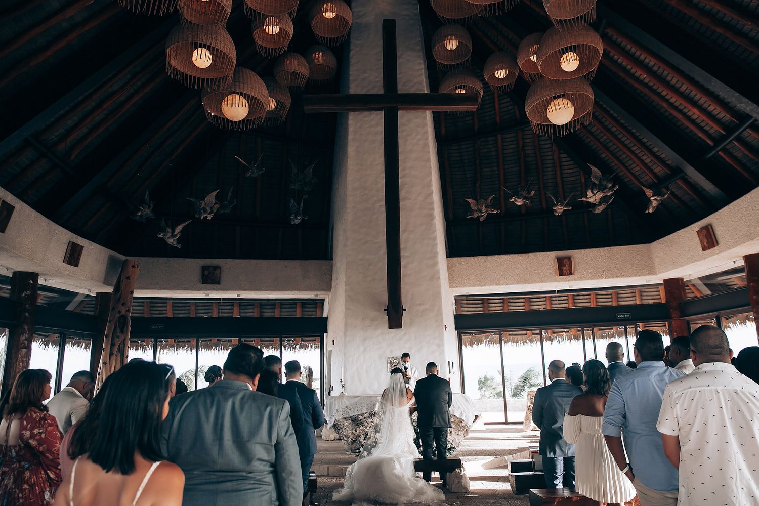 Wedding ceremony taking place in an octagonal pavilion with hanging lights and gathered guests.