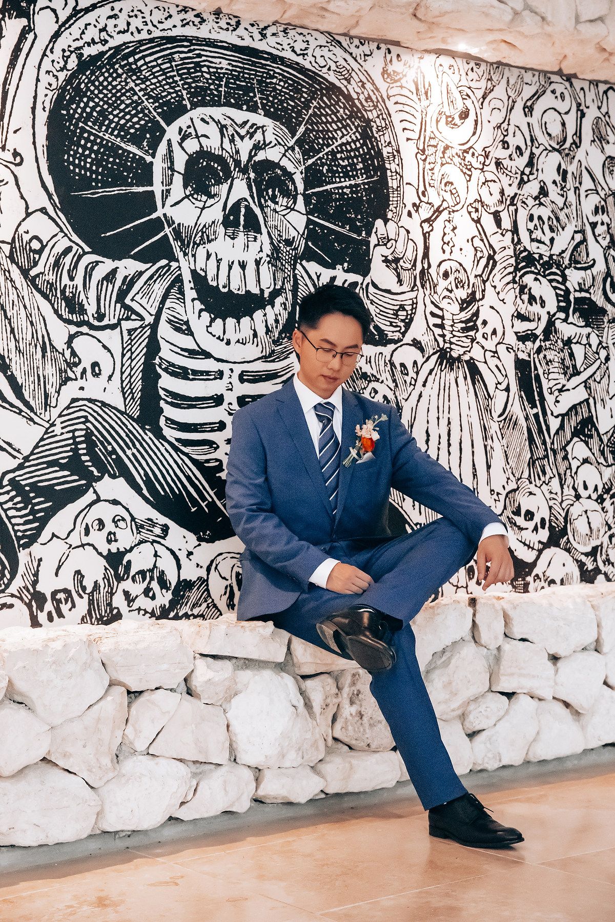 Groom in navy suit poses against artistic black and white wall mural backdrop during wedding photoshoot.