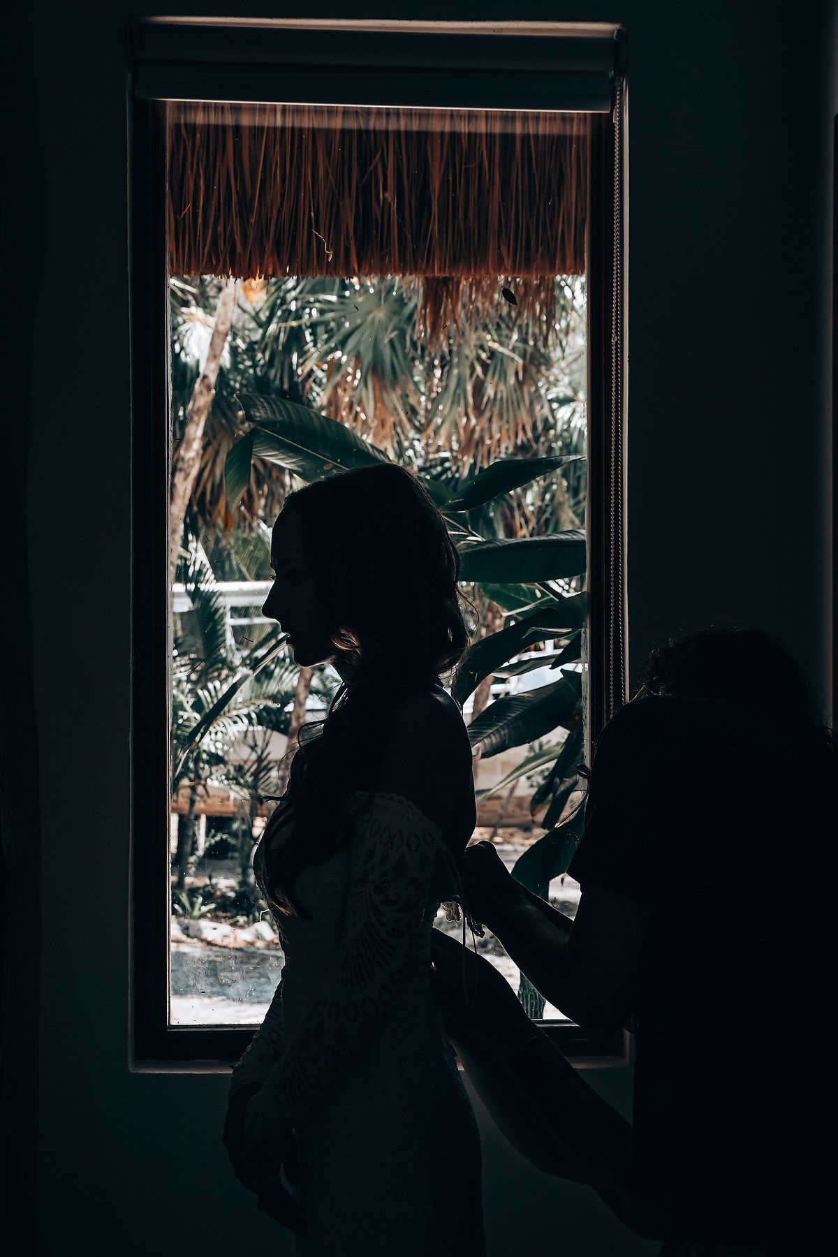 Dark silhouette figure drinks from a cup against a window with decorative patterns in moody lighting.