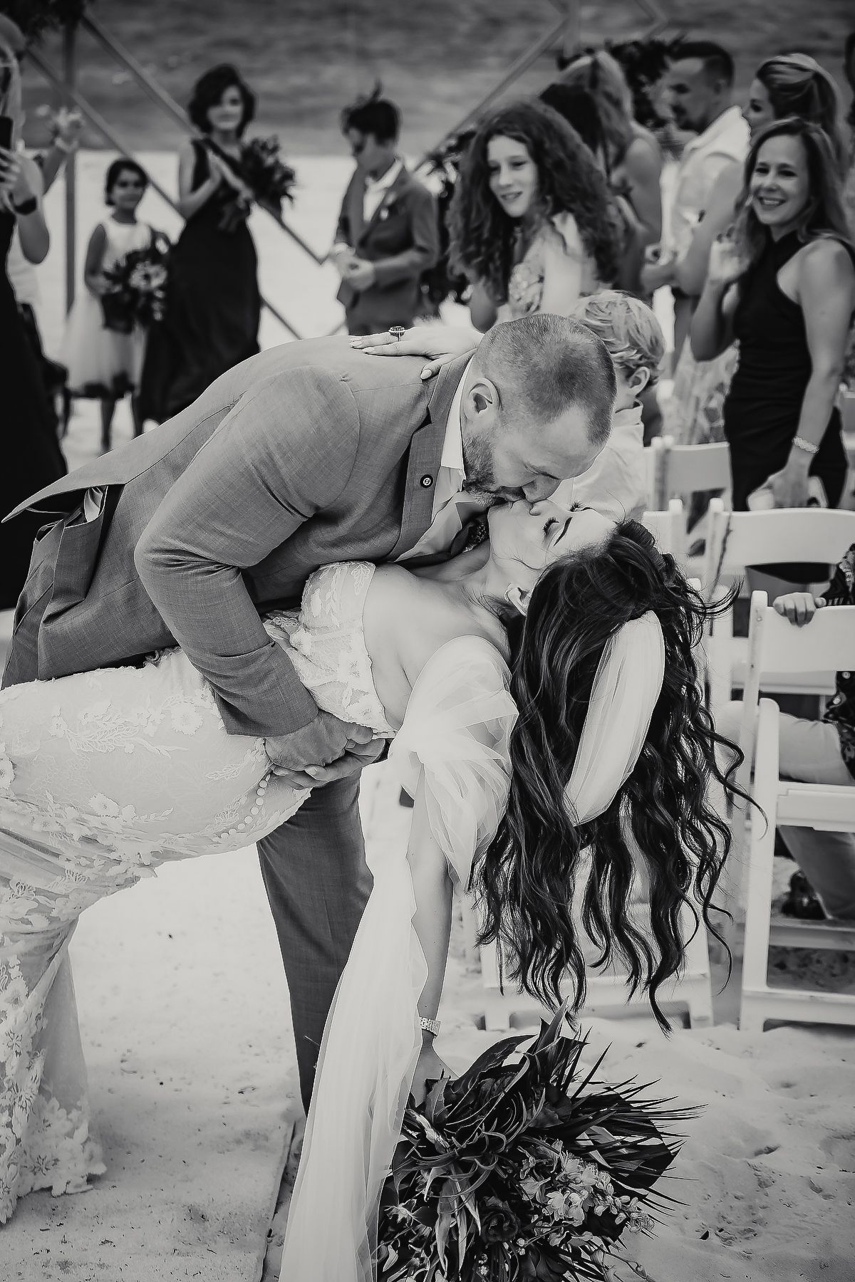 Groom dips bride for a romantic kiss at beach wedding ceremony in black and white photo.