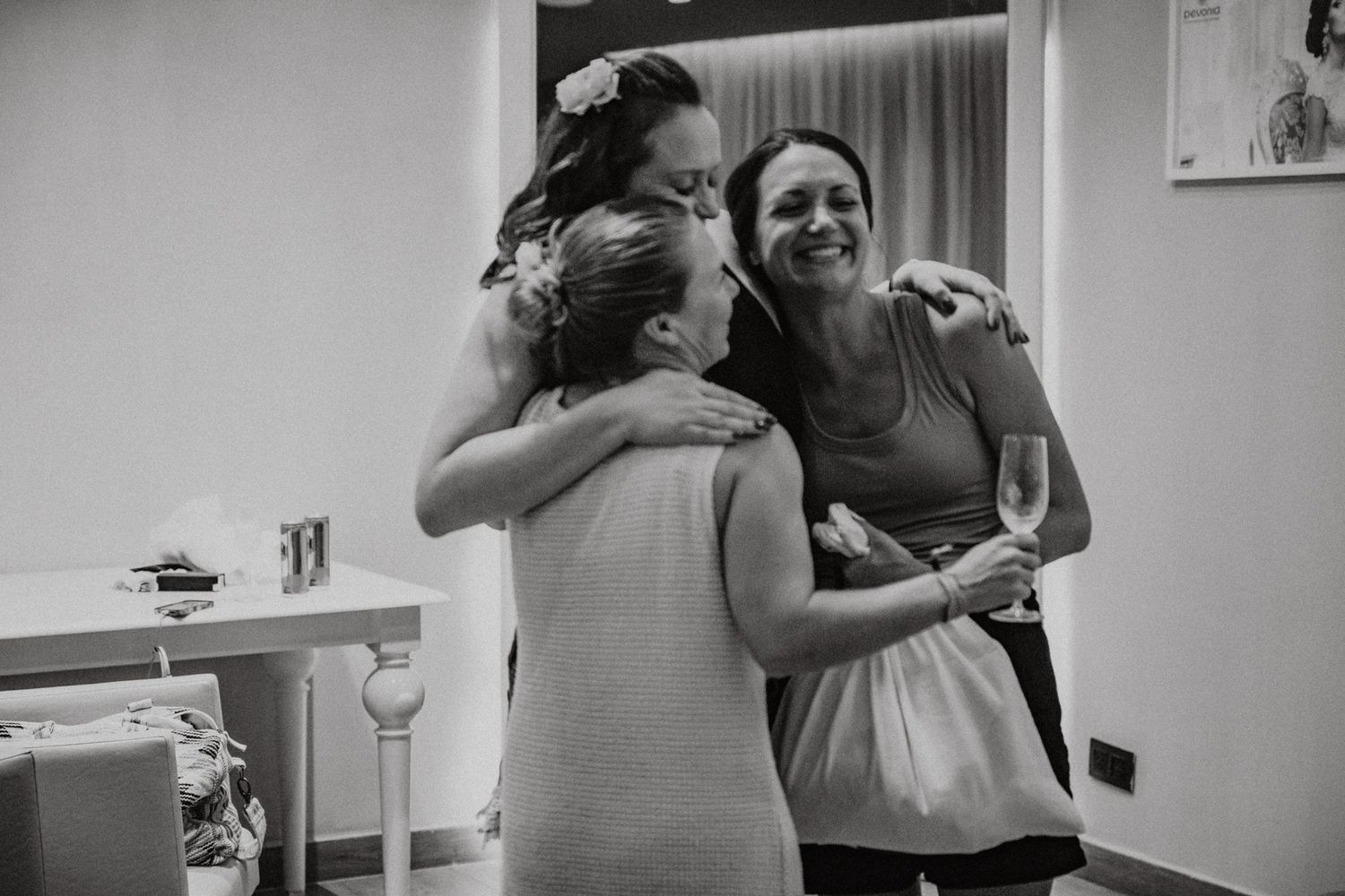 Black and white photo of three women sharing a warm group hug during a joyful wedding celebration.