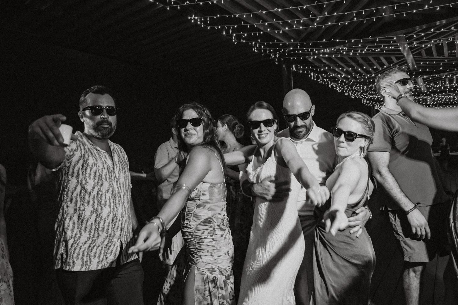 Black and white photo of wedding guests dancing and posing together at an outdoor reception.