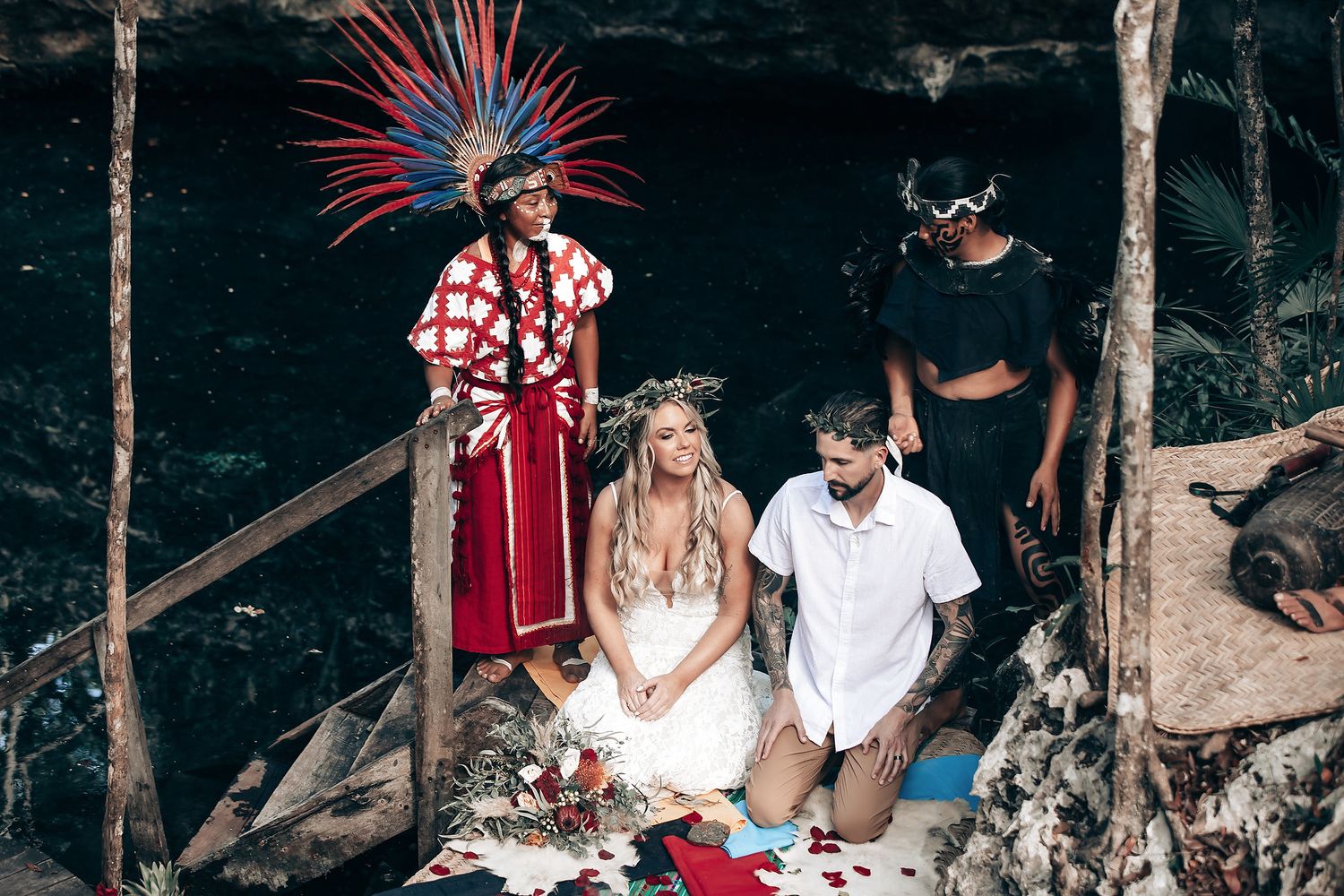 A wedding ceremony takes place in a tropical beach setting with red and white decorative elements.