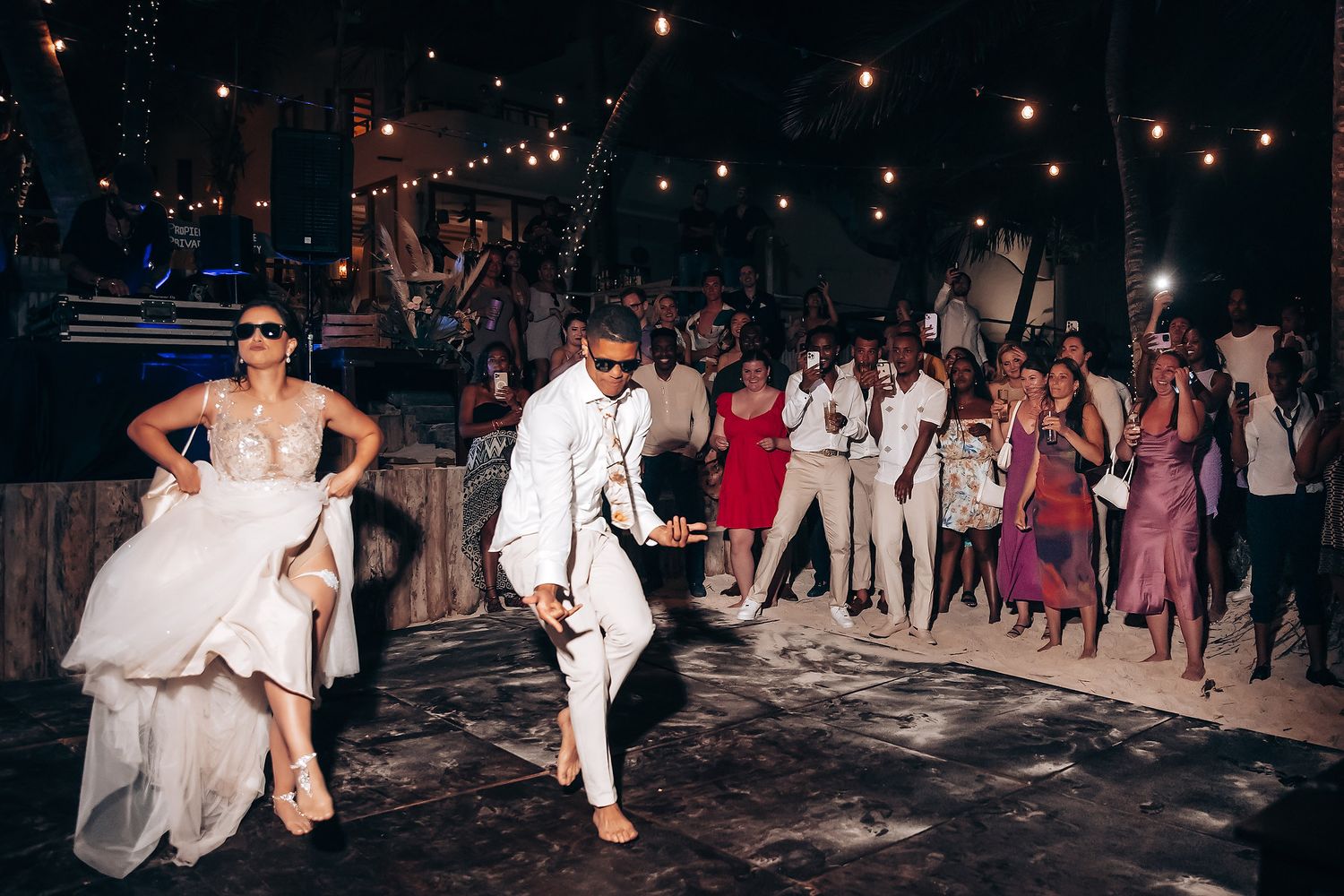 Couples dancing at a nighttime beach wedding reception under twinkling lights.
