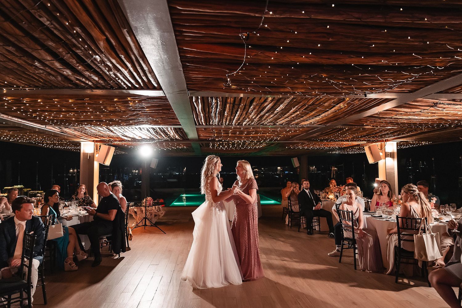 Panoramic view of wedding reception space with twinkling lights and wooden ceiling beams.