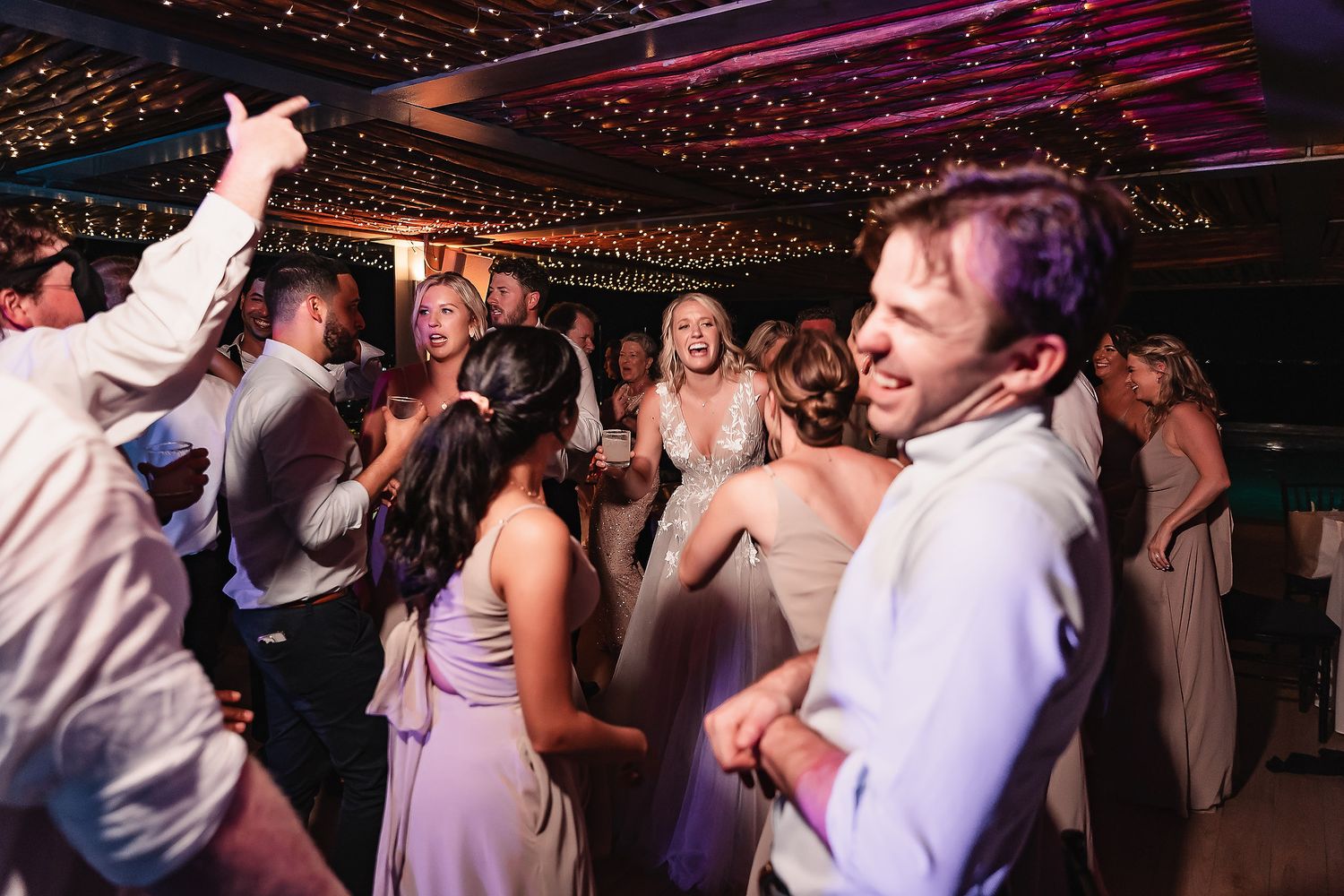 Wedding guests dancing under colorful lights at an evening reception celebration.