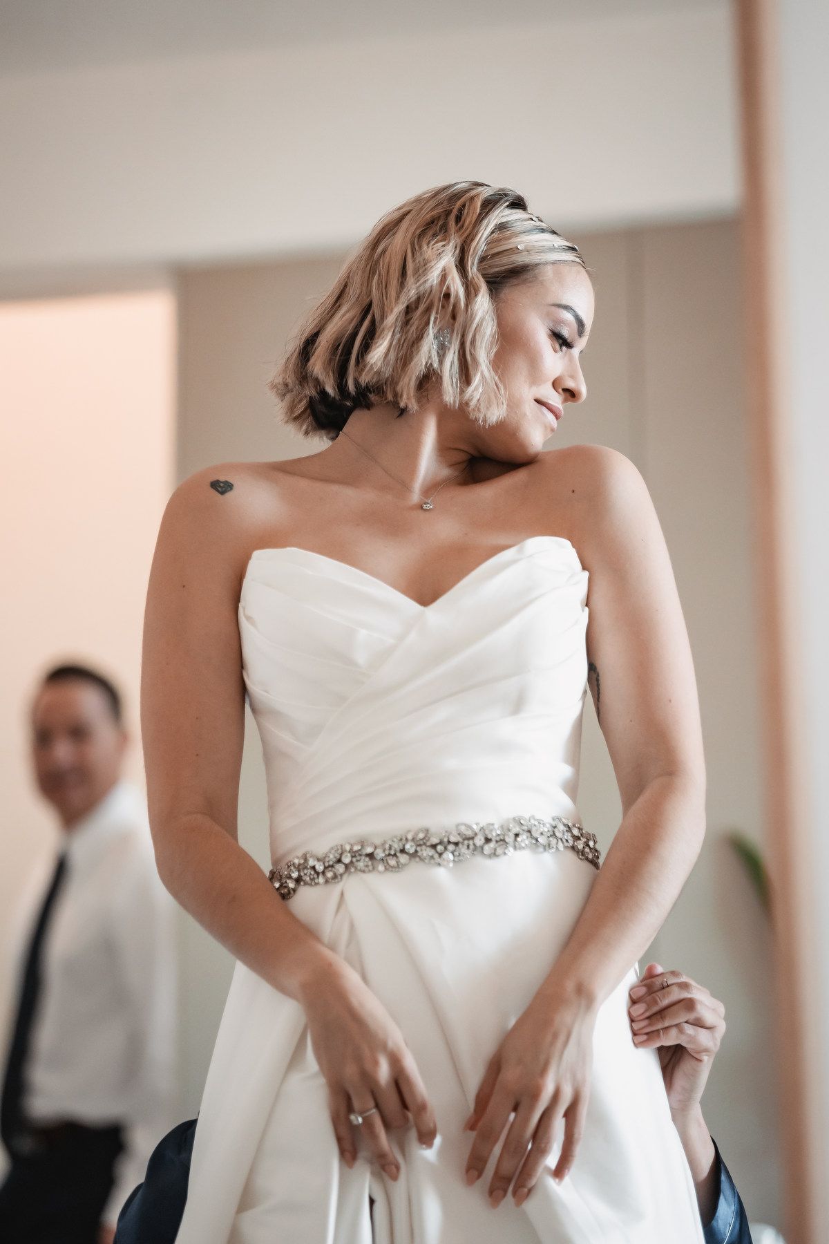 Beautiful bride in strapless white gown with crystal belt looking down elegantly.