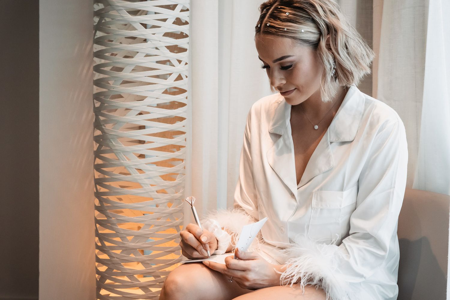 Woman in white shirt writing notes beside decorative lattice lamp.