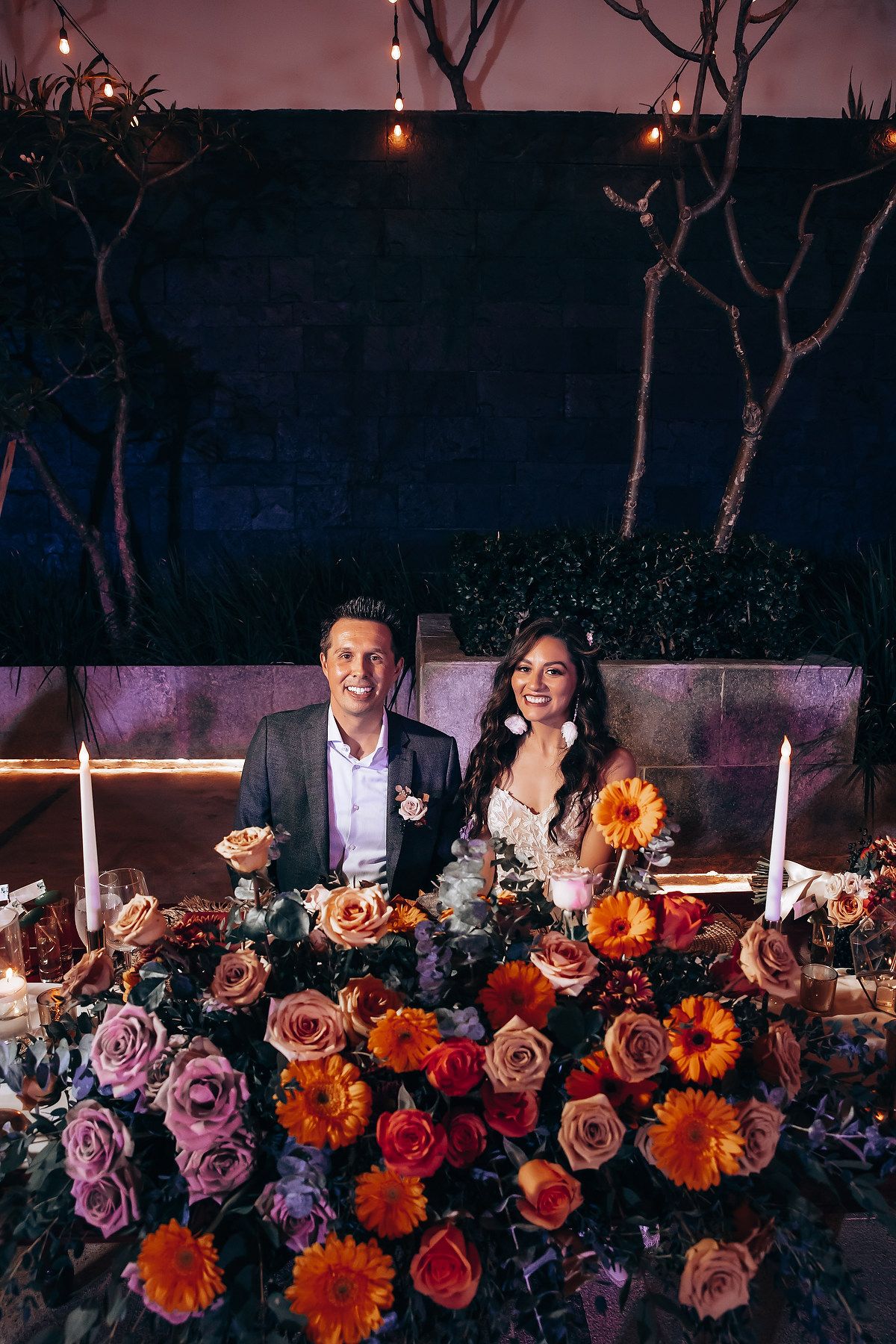 Evening wedding reception table decorated with vibrant roses and floral arrangements.