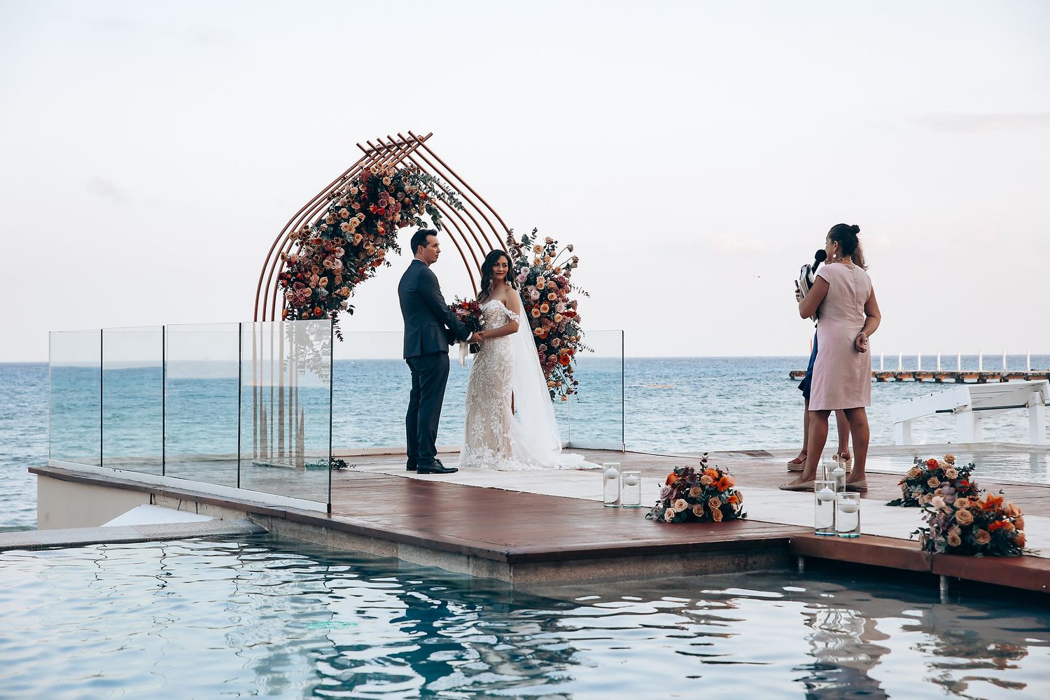 A couple shares an intimate moment during their waterfront wedding ceremony on a pier with floral decorations.