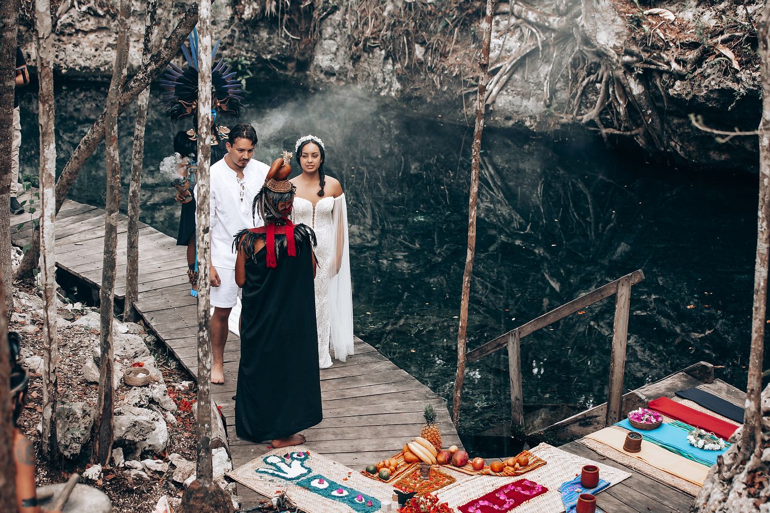 Wedding ceremony participants gather on a rustic wooden platform surrounded by natural rock formations and trees.