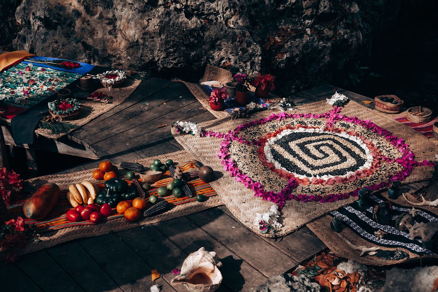 Colorful Mexican decorations and floral arrangements laid out on stone ground for a traditional ceremony.