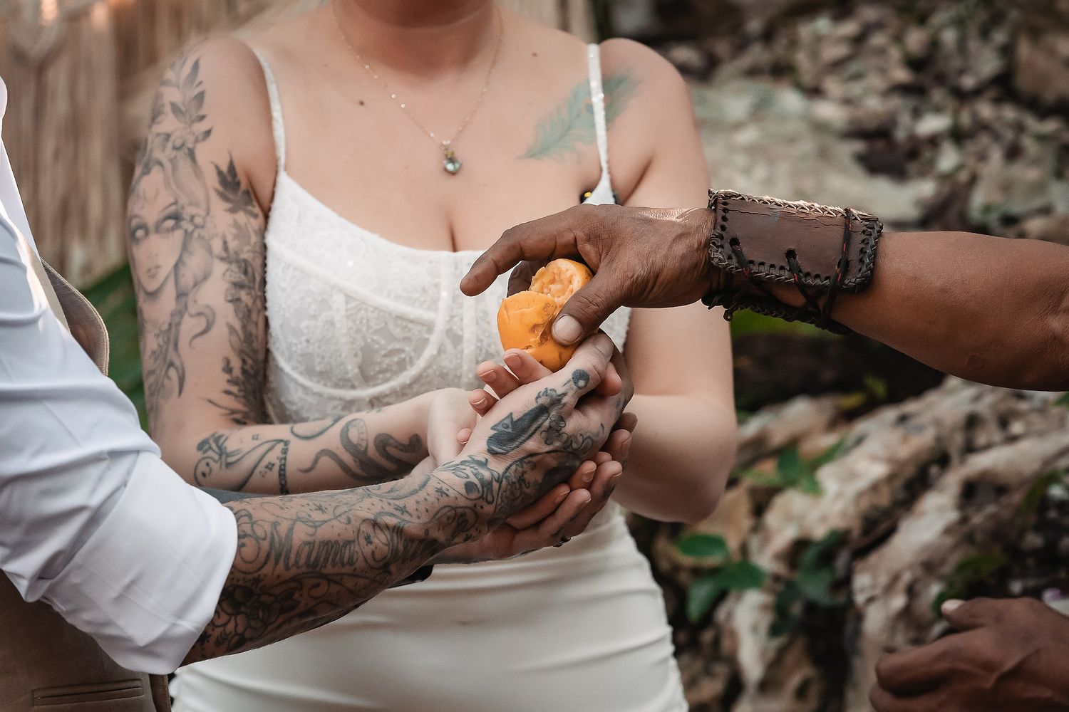 Tattooed couple sharing an orange fruit during an outdoor wedding ceremony ritual.