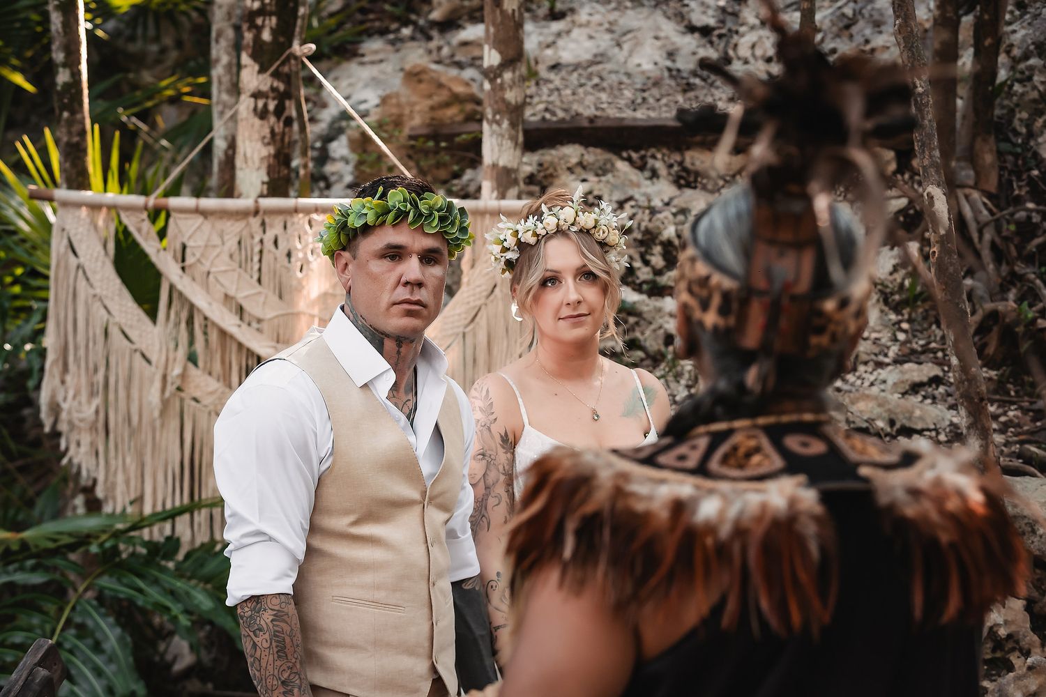 Couple in floral crowns exchanging vows at a tropical jungle wedding ceremony with macrame backdrop.