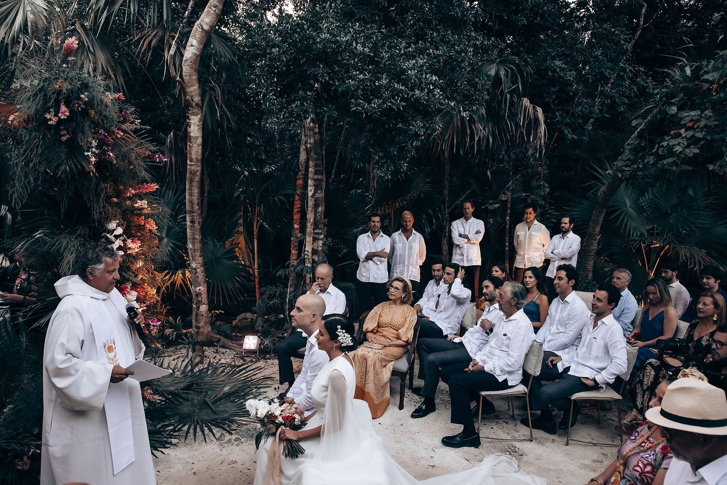 An intimate outdoor wedding ceremony surrounded by lush tropical foliage and palm trees.