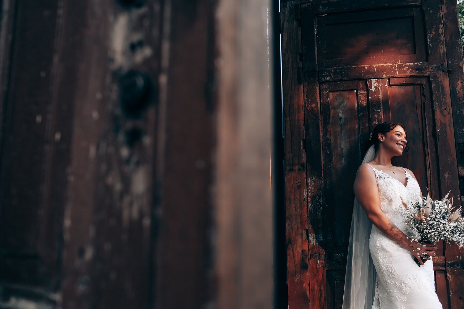 Moody wedding portraits with dramatic lighting against dark wooden structures.