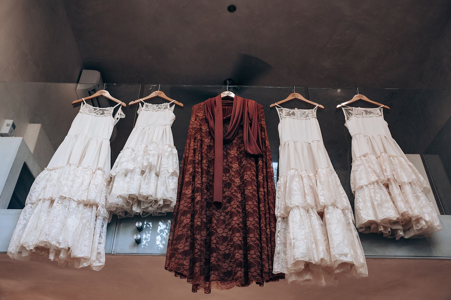 Vintage-style dresses in burgundy and cream colors hang on wooden hangers against a dark background.