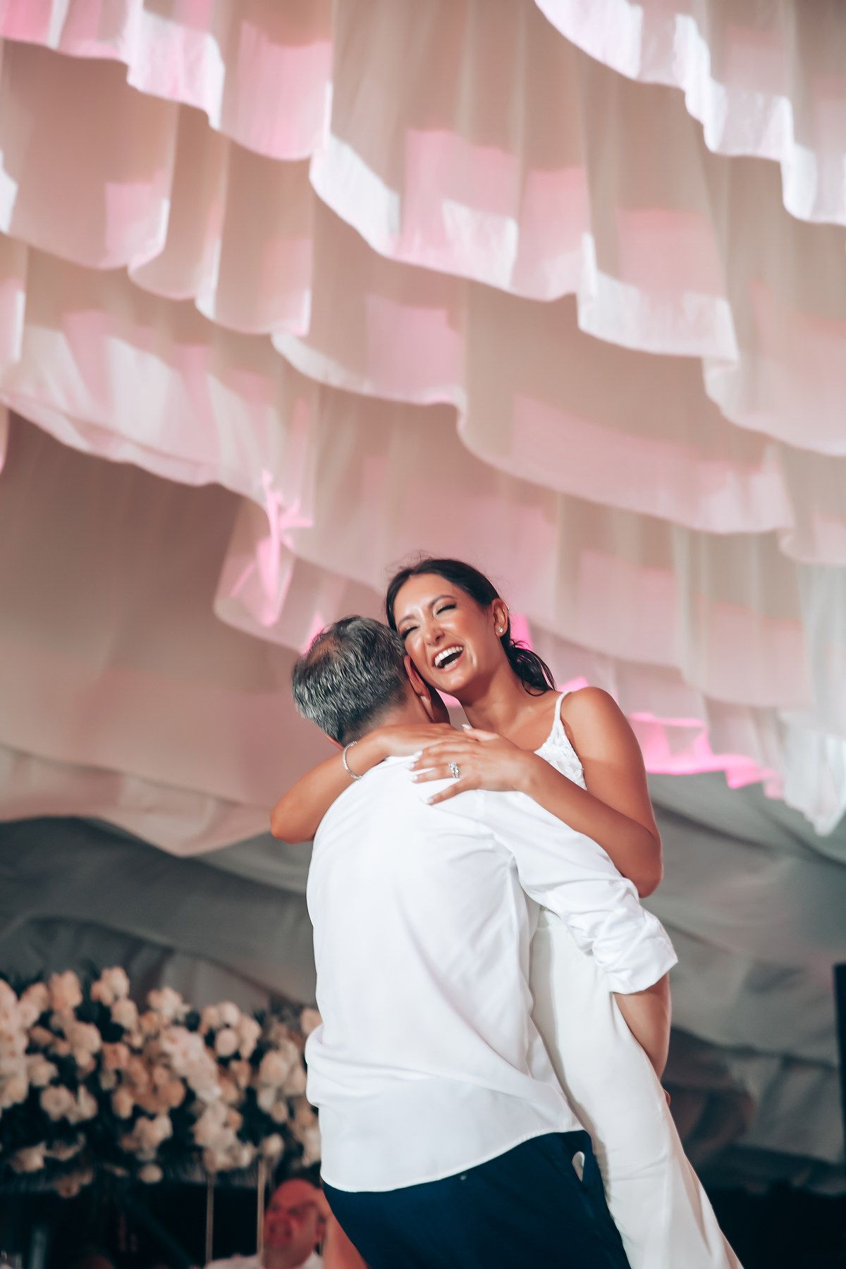 A joyful dance sequence captured in a wedding tent with pink drapery and floral decorations.