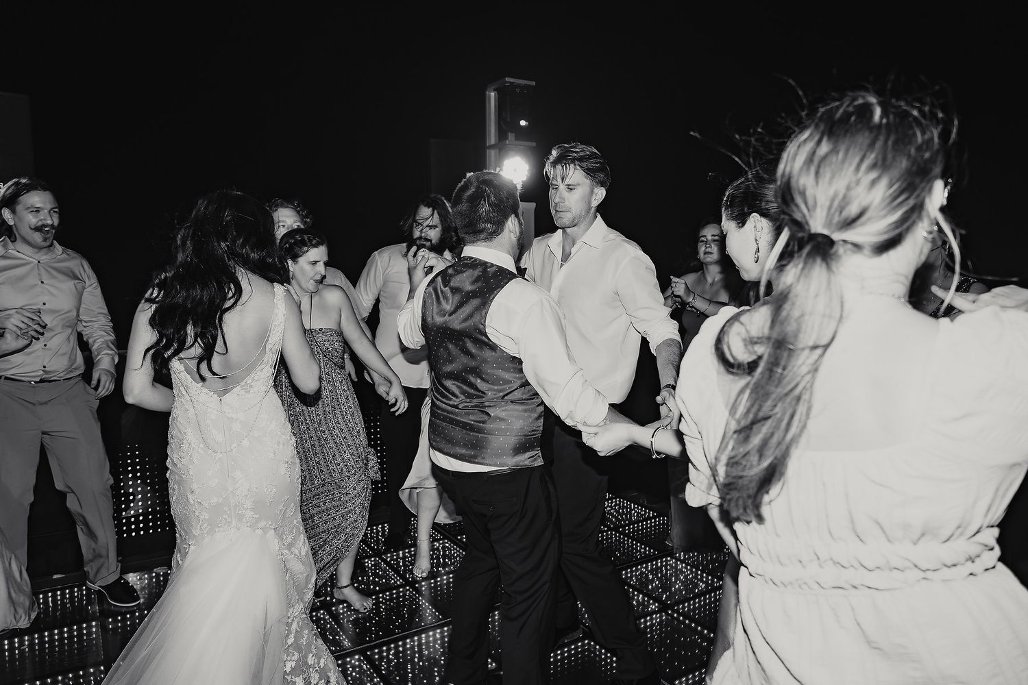 Black and white wedding reception dance floor photo with bride, groom, and guests celebrating together.