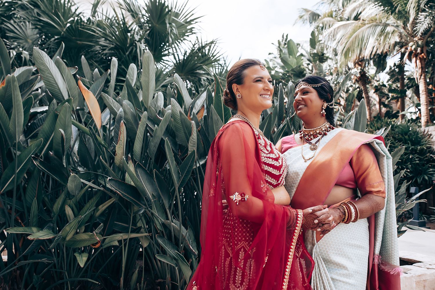 Two people in traditional Indian attire stand together in a tropical garden setting.