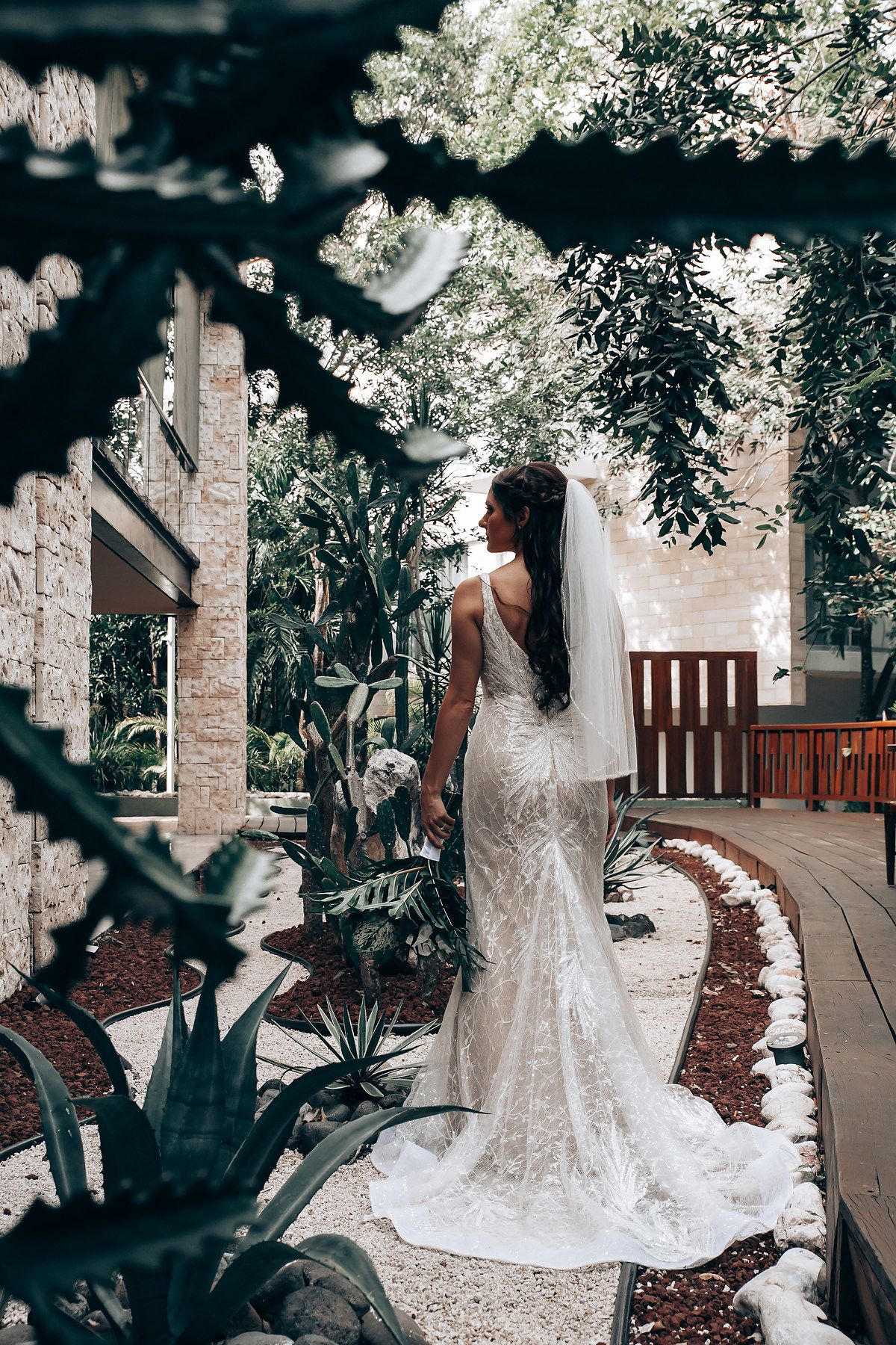 Stunning lace wedding gown with long train photographed in a garden setting with brick and wooden details.