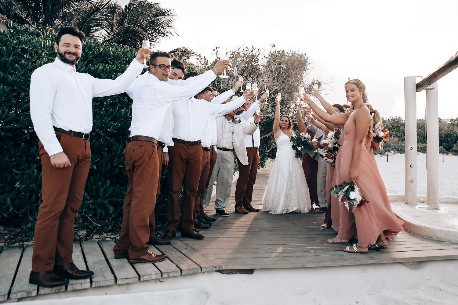 Wedding party in brown and white attire poses on a paved walkway at an outdoor venue.