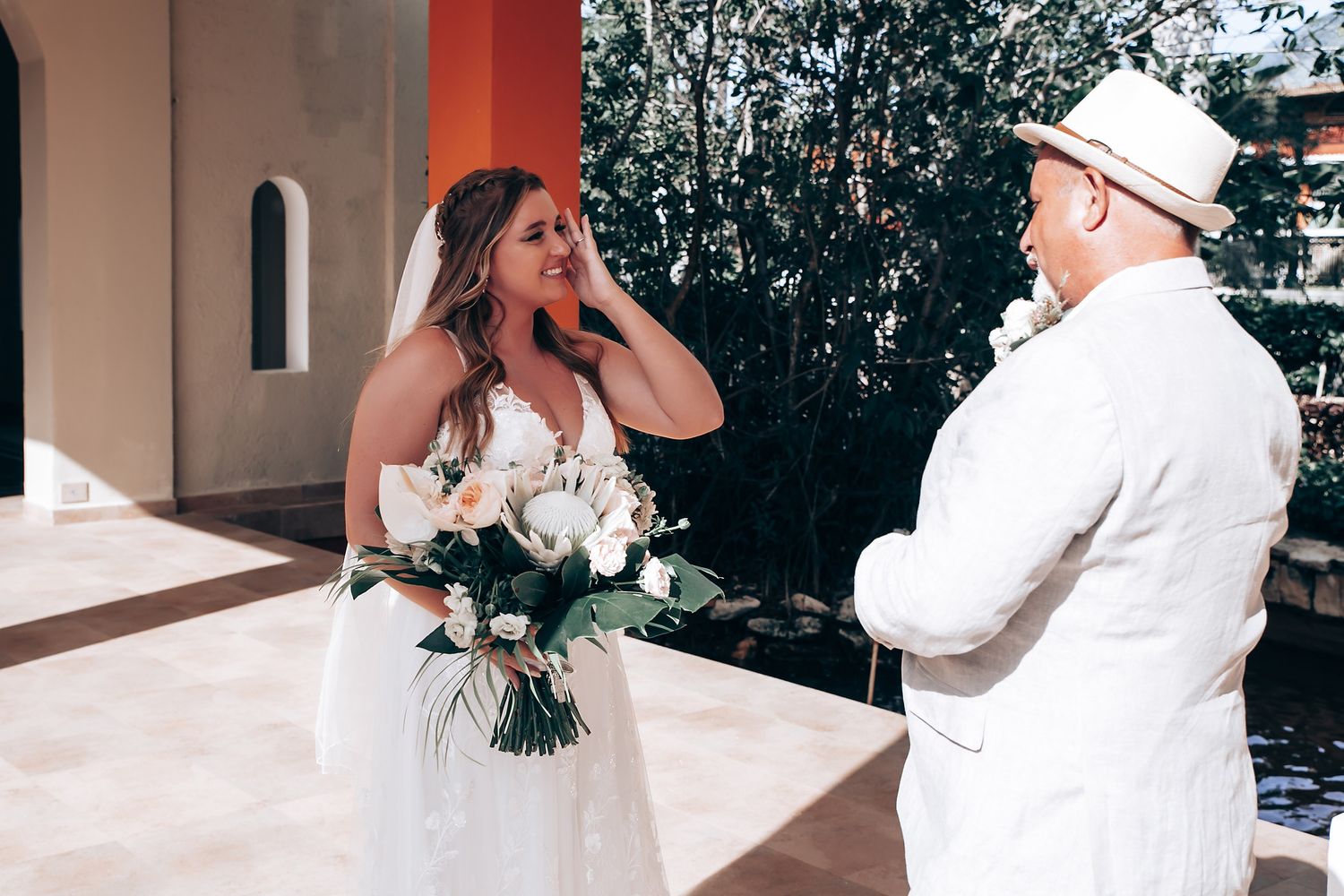A bride in a white wedding dress holds a bouquet while sharing an emotional moment with someone in white attire.