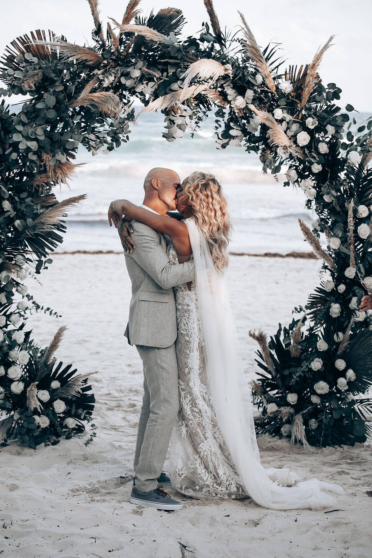 Romantic beach wedding moment under a floral arch by the ocean.