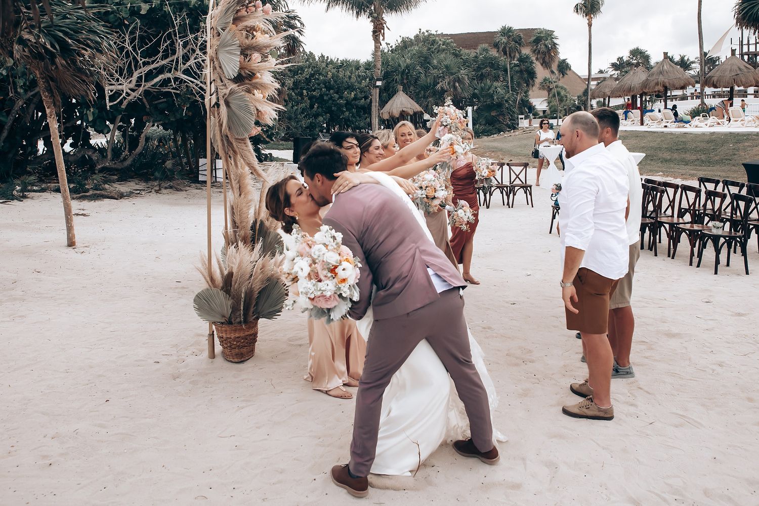 Newlyweds dance playfully on sandy beach during wedding celebration.