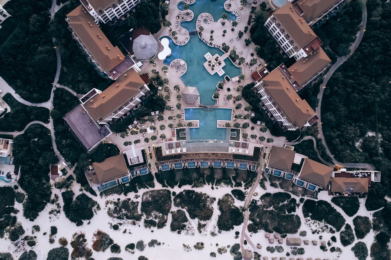 An aerial view of a resort-style hotel with a large swimming pool surrounded by buildings.