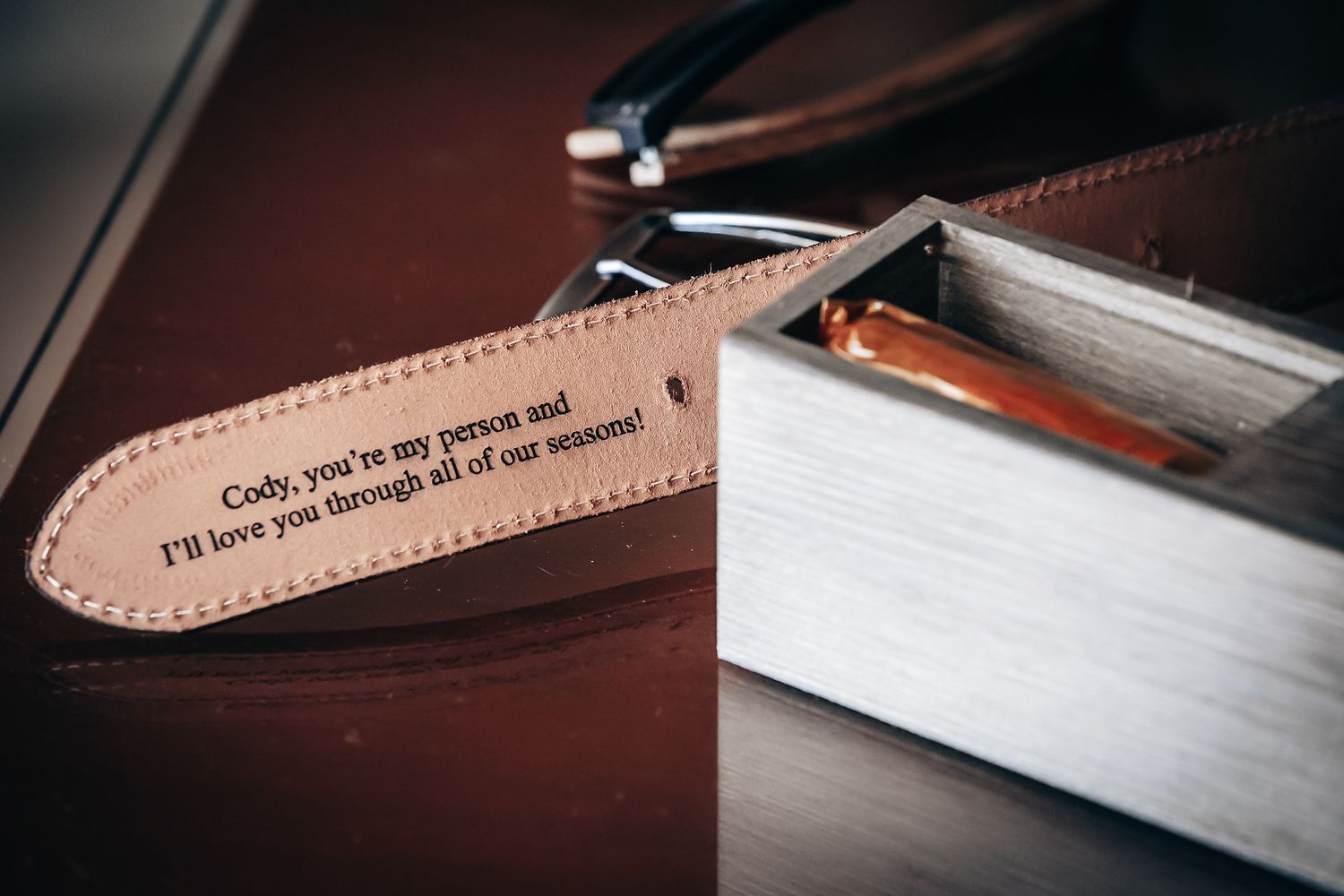A leather tag with an inspirational message is attached to a pair of scissors on a wooden surface.