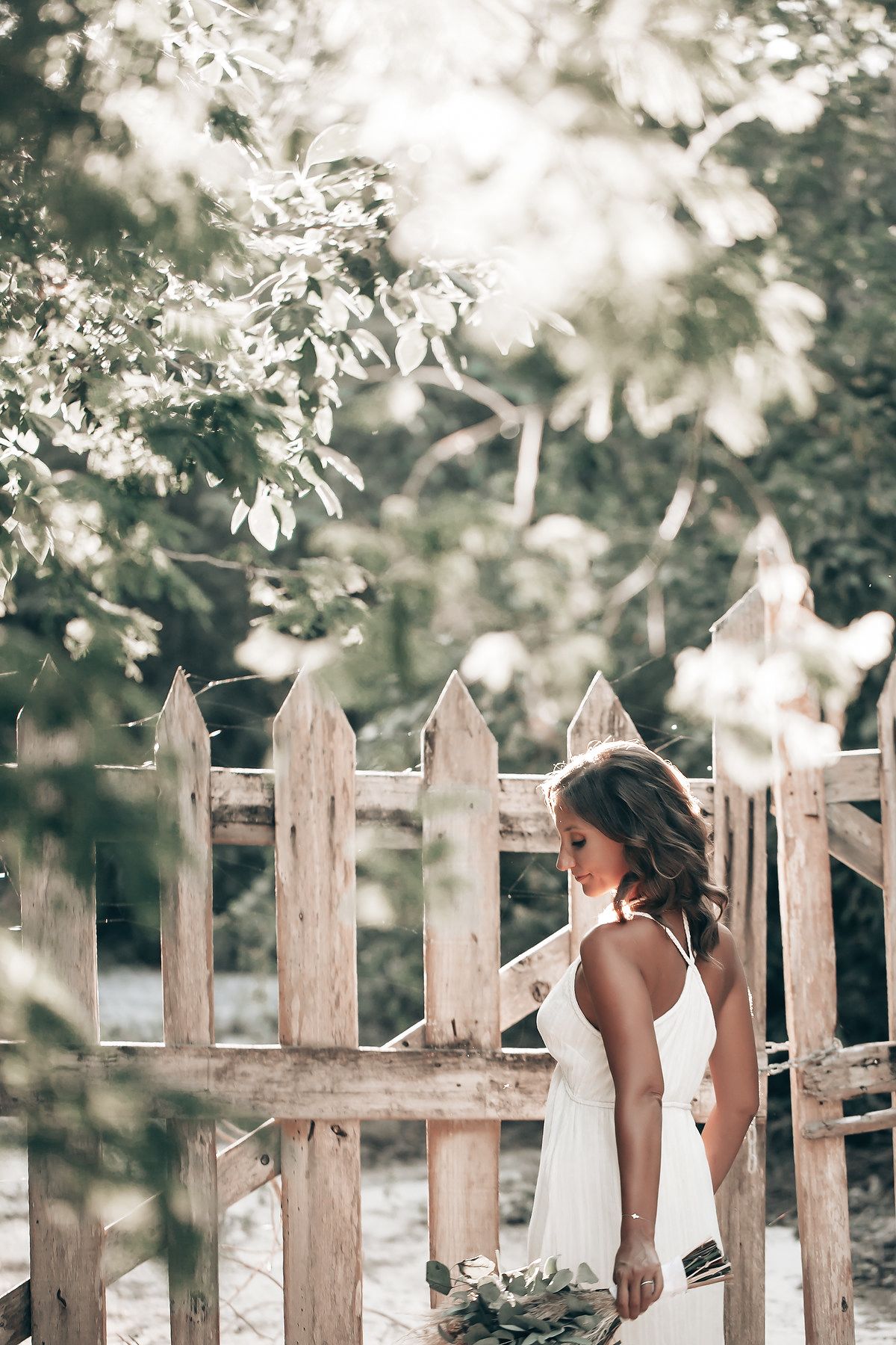 A woman stands in a tropical forest setting, surrounded by a wooden fence and lush foliage.