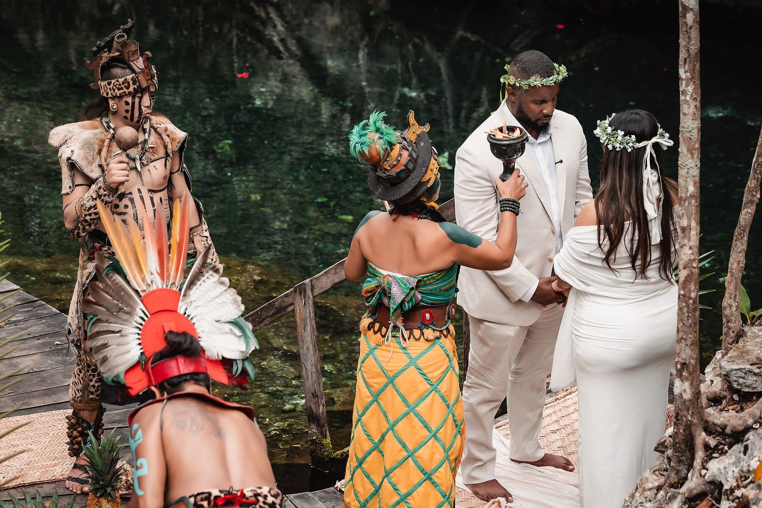 Mayan ceremony wedding with officiant in traditional attire blessing couple in white at a cenote in Mexico.