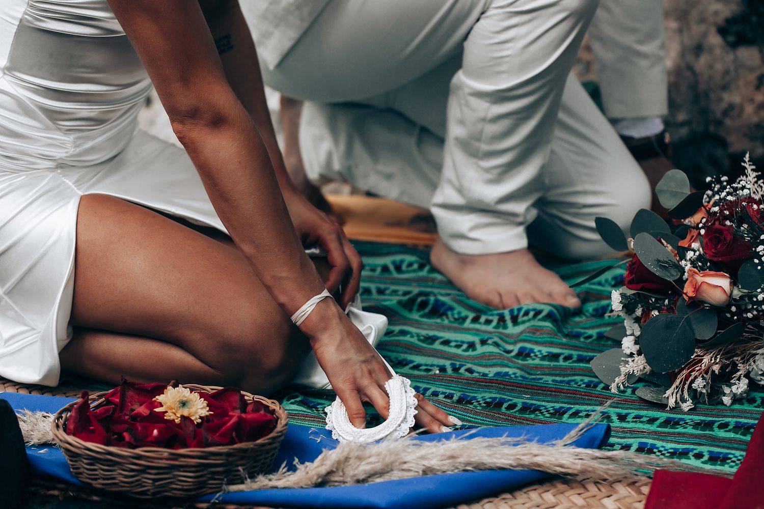 Traditional ceremonial objects and flowers arranged on a teal textile during a ritual.