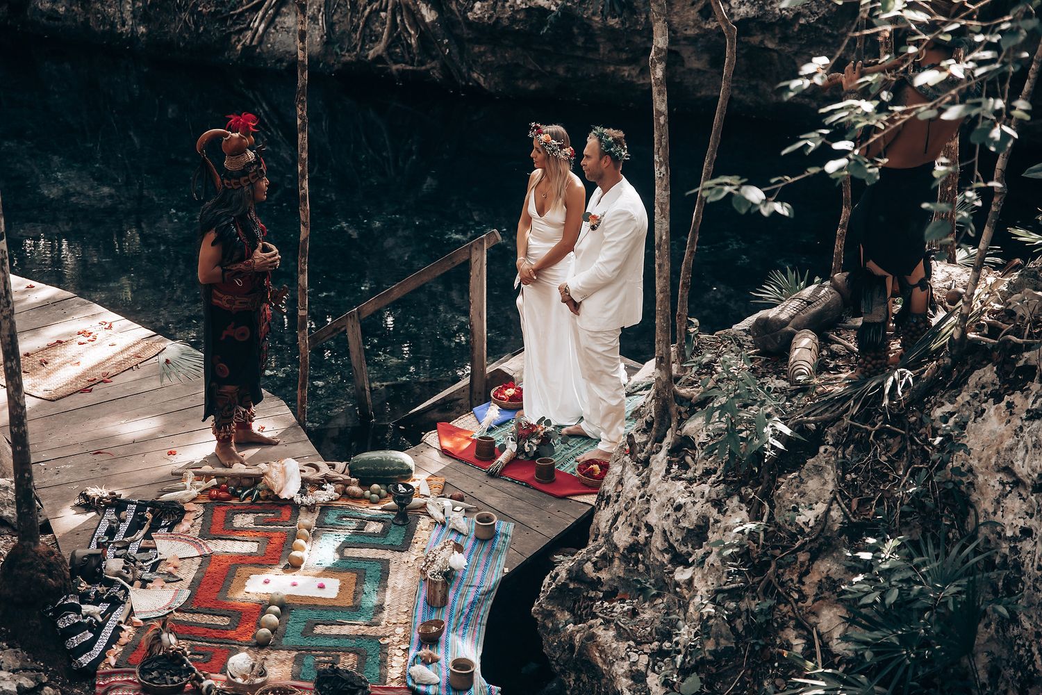 A wedding ceremony in a tropical forest setting with traditional Mayan elements and decorative rugs.