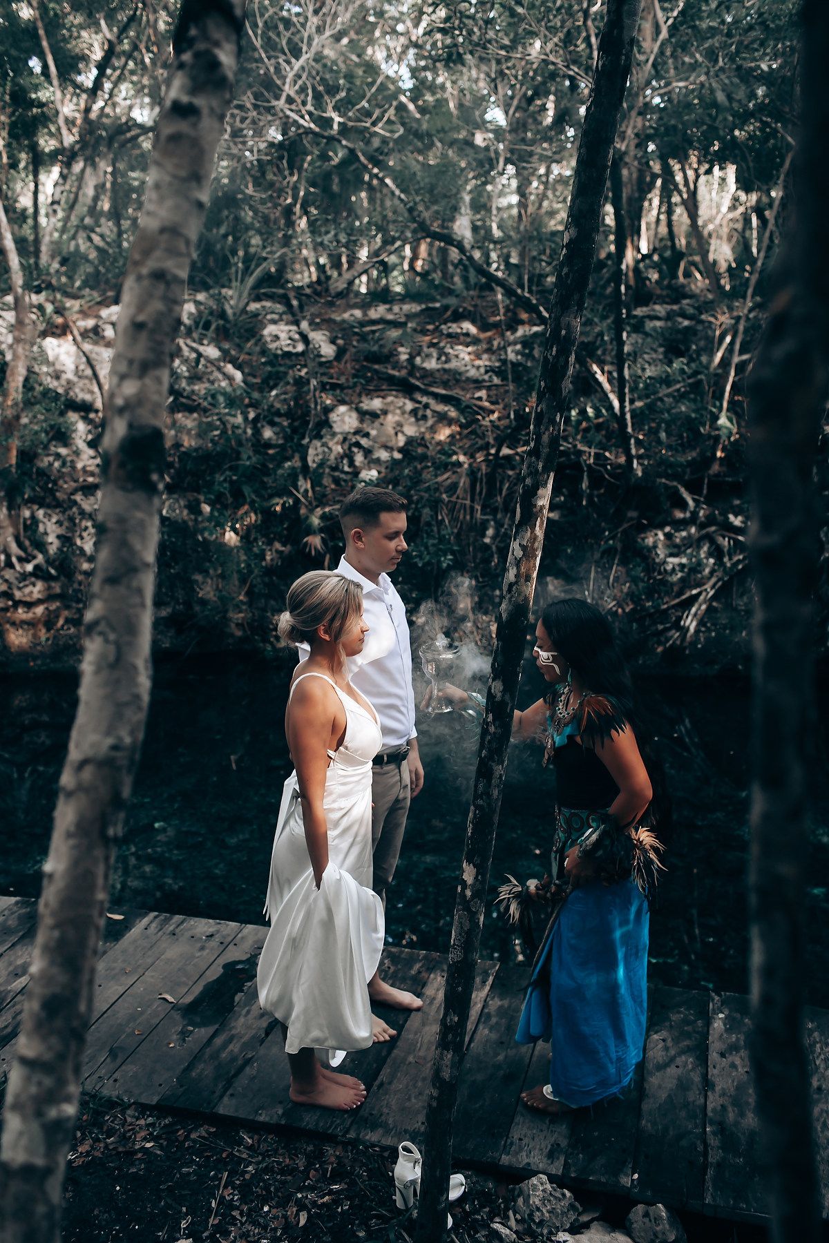 Intimate wedding ceremony setup on wooden platform in a mystical cave surrounded by trees.