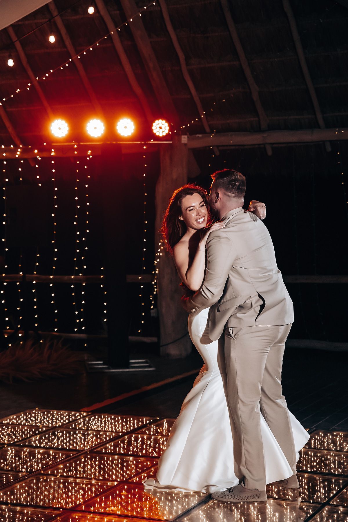 Couple sharing their first dance in an elegant barn setting with romantic string light decorations.
