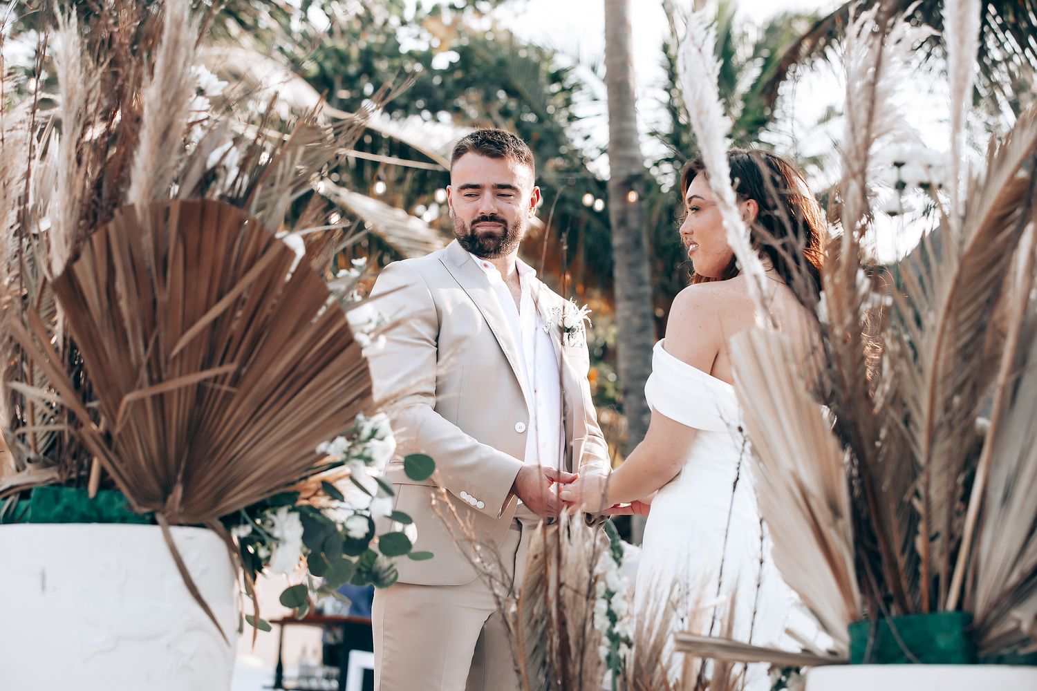 Wedding party celebrates with dried palm leaf fans outdoors in a natural setting with trees in the background.