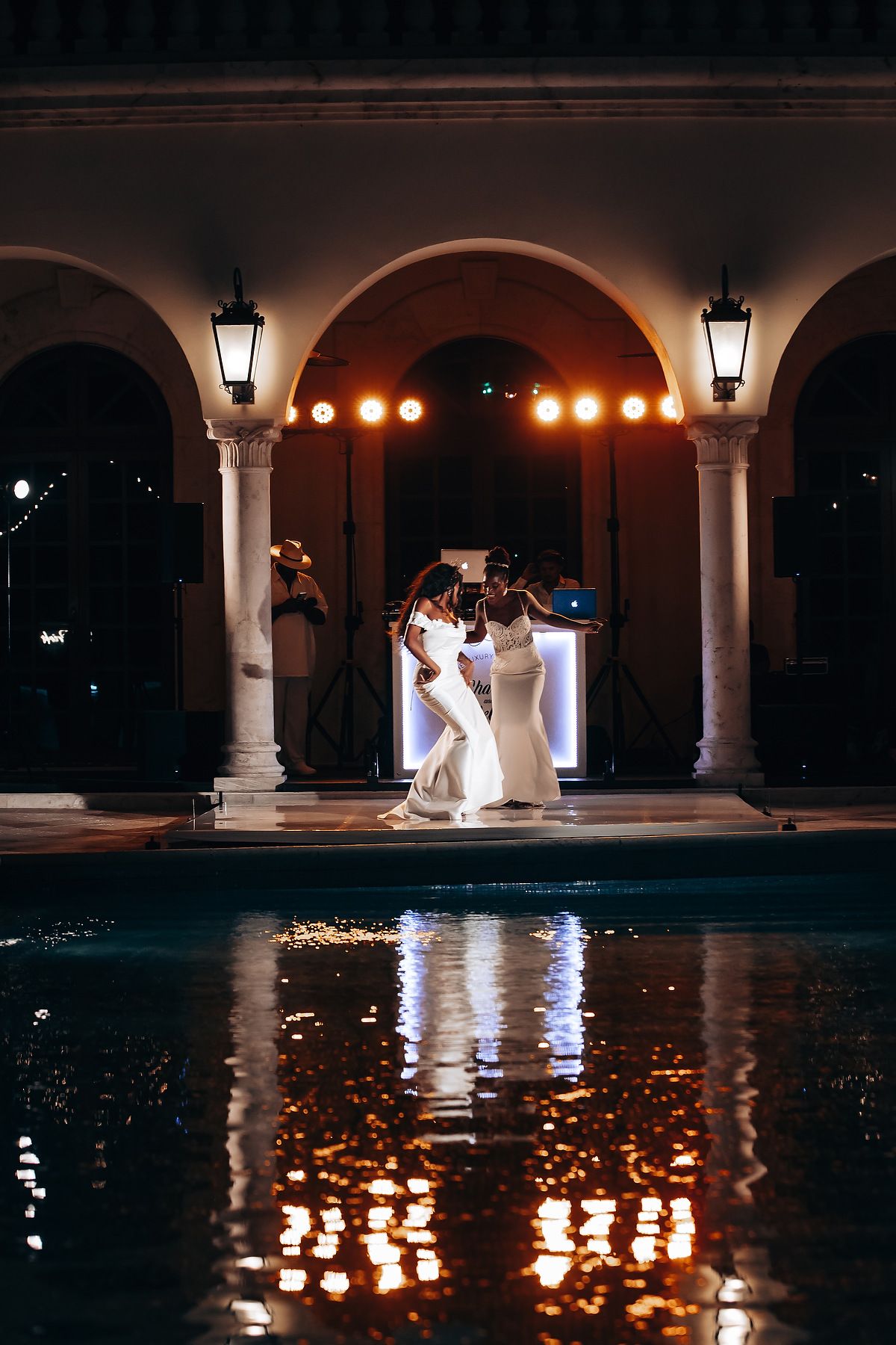 Nighttime wedding photos by a pool with arched columns and romantic lighting reflections.