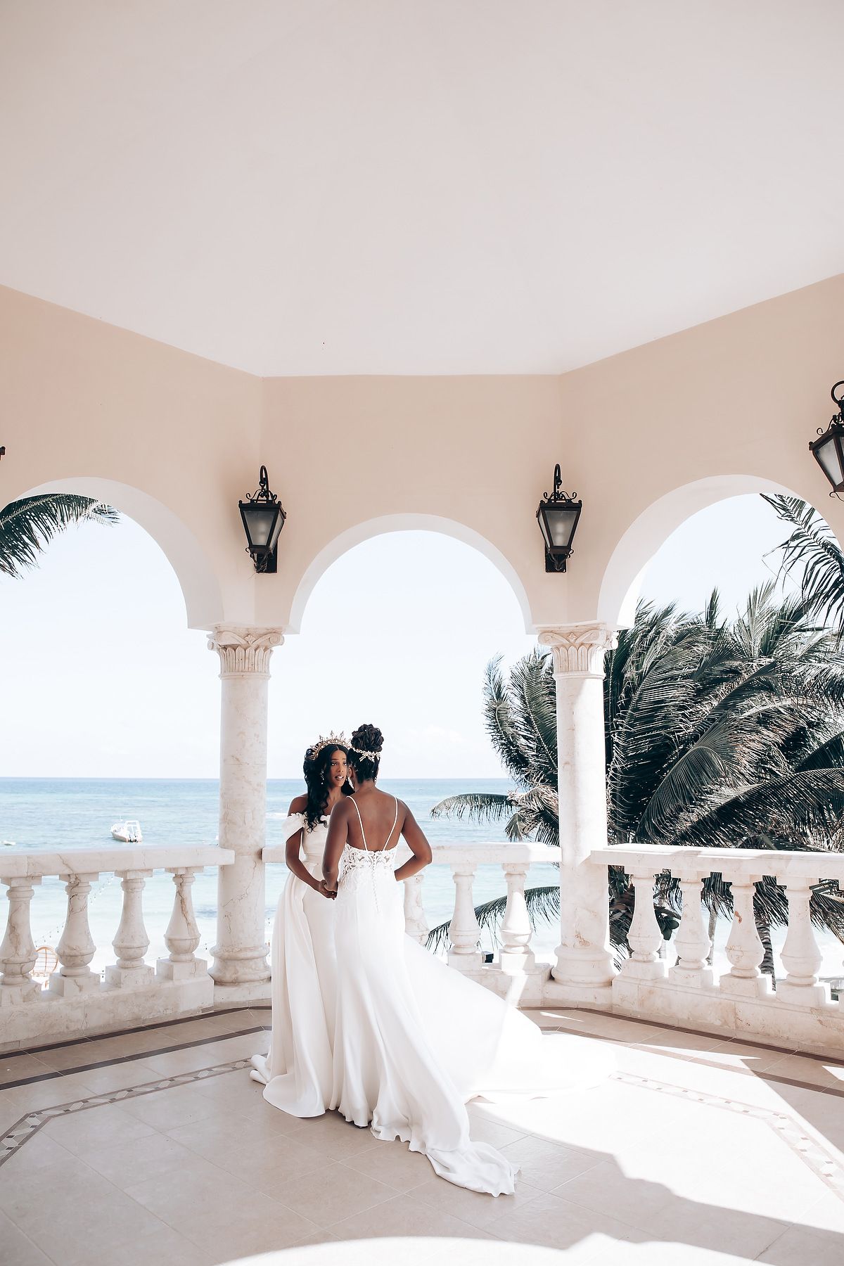 Romantic wedding photoshoot on a white Mediterranean-style balcony with arched columns overlooking the ocean.