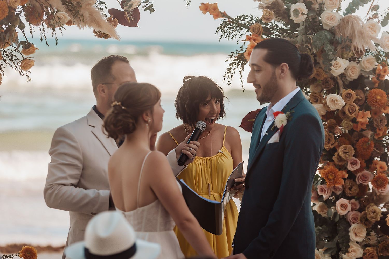 Intimate wedding ceremony under an autumn-colored floral arch by the beach.