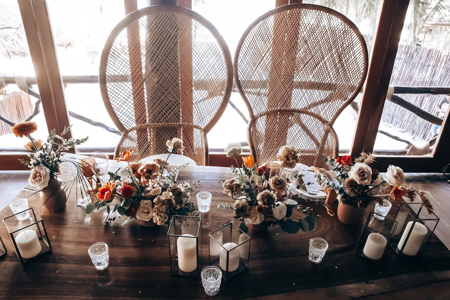 Elegant wedding reception table decor with floral arrangements and glowing candles under rustic wooden beams.