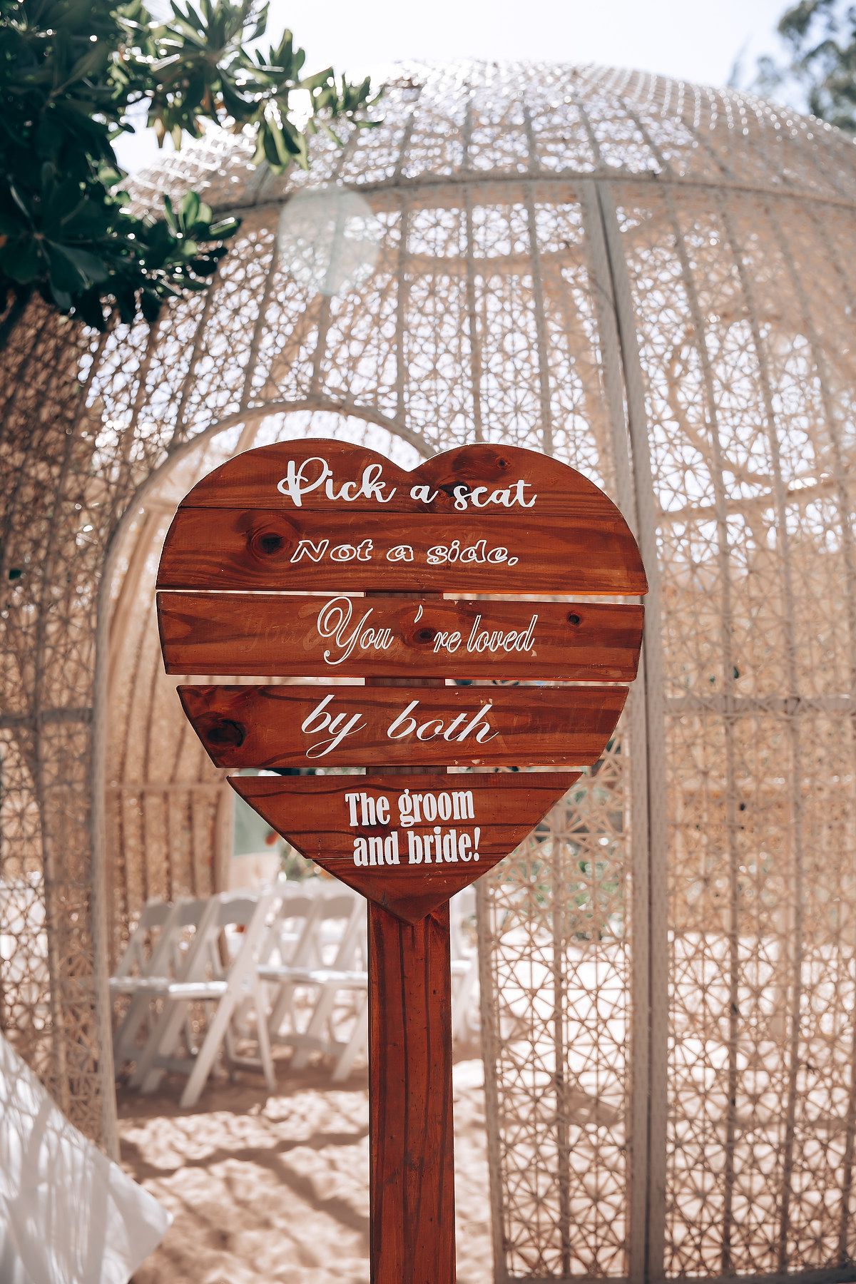 Wooden heart-shaped wedding signs with text displayed at rustic outdoor ceremony.