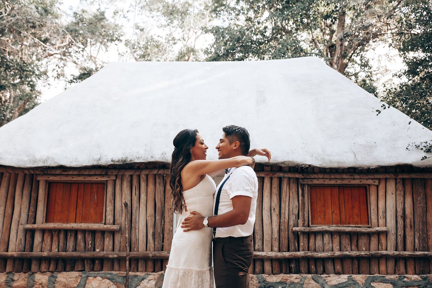 Couple sharing a romantic kiss in front of a rustic wooden fence during their wedding celebration.