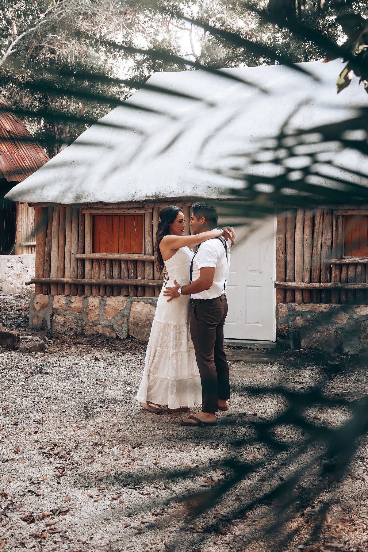 A romantic couple in light and dark attire share an intimate moment against a rustic wooden fence backdrop.