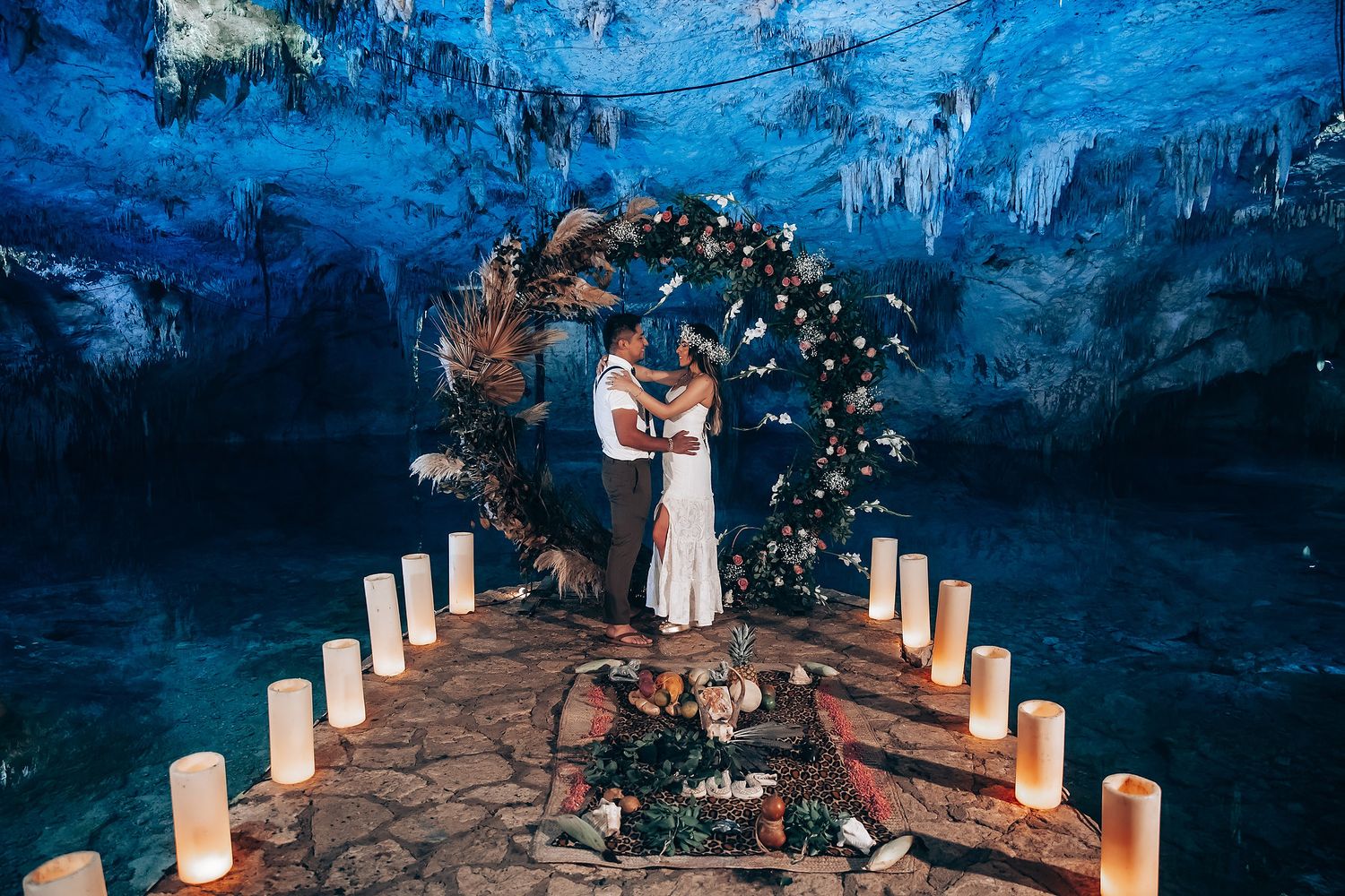 Luminous cave wedding ceremony setup with glowing candles lining a stone pathway and blue-lit rock formations.