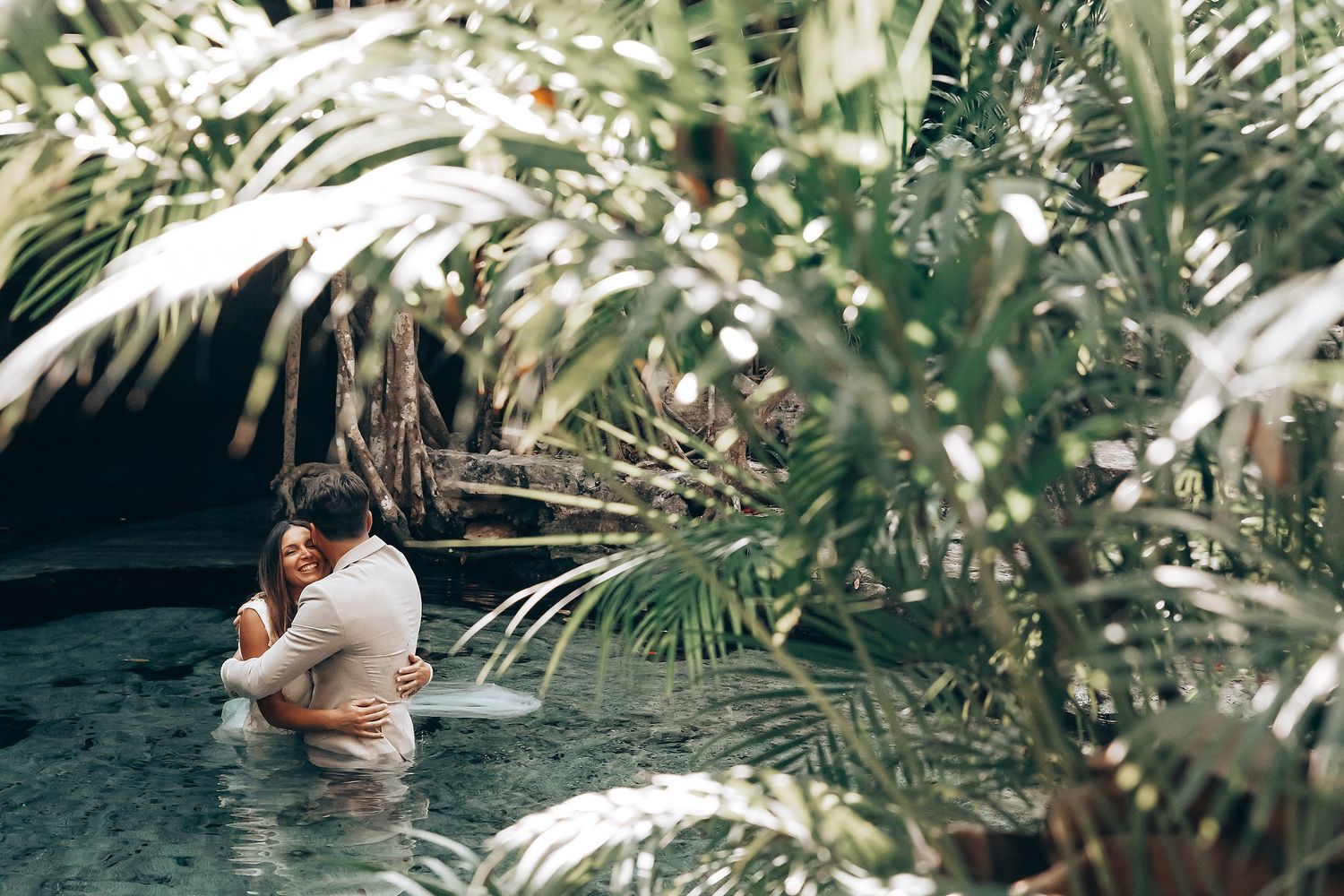 An intimate wedding moment photographed in a lush garden setting with palm fronds.